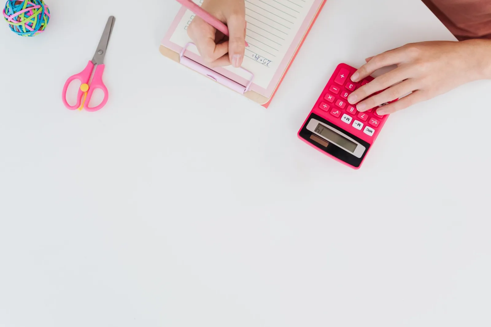 Top view of student calculating with a pink calculator and writing notes, featuring educational tools.
