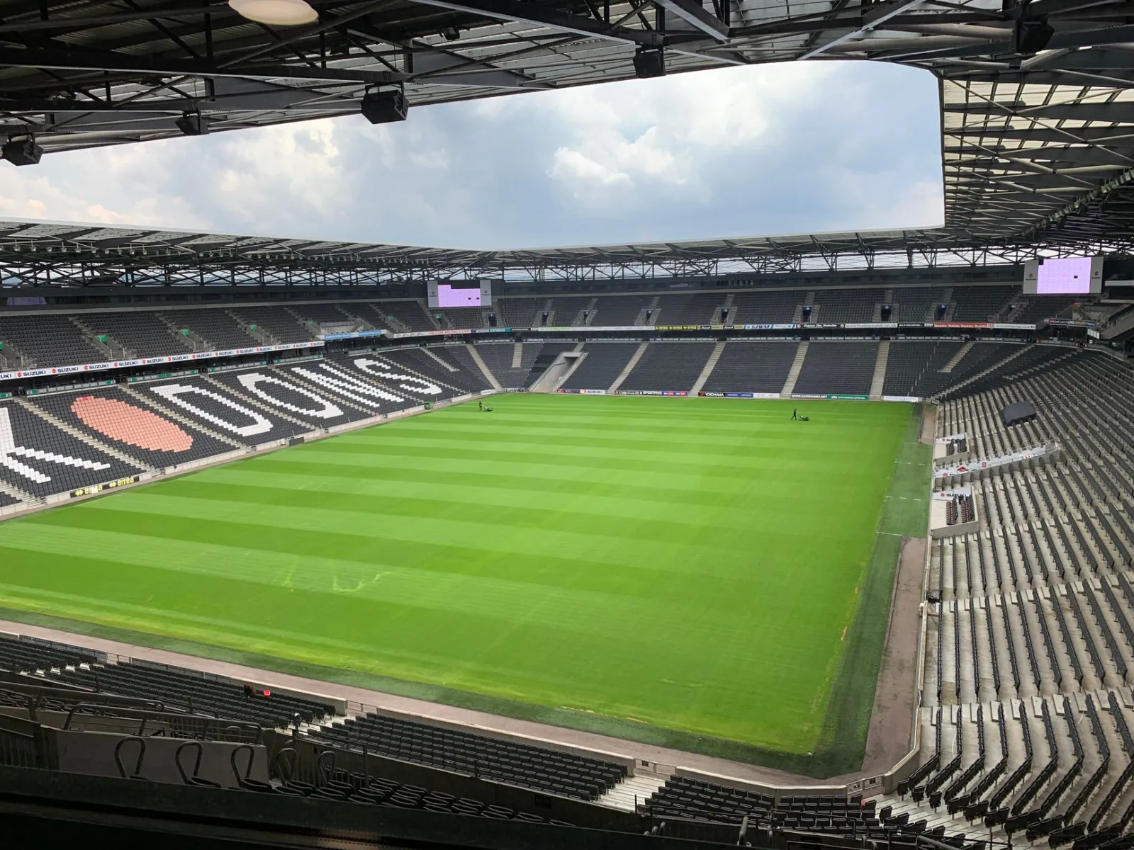 Empty soccer stadium with lush green field and seating, captured during the day.