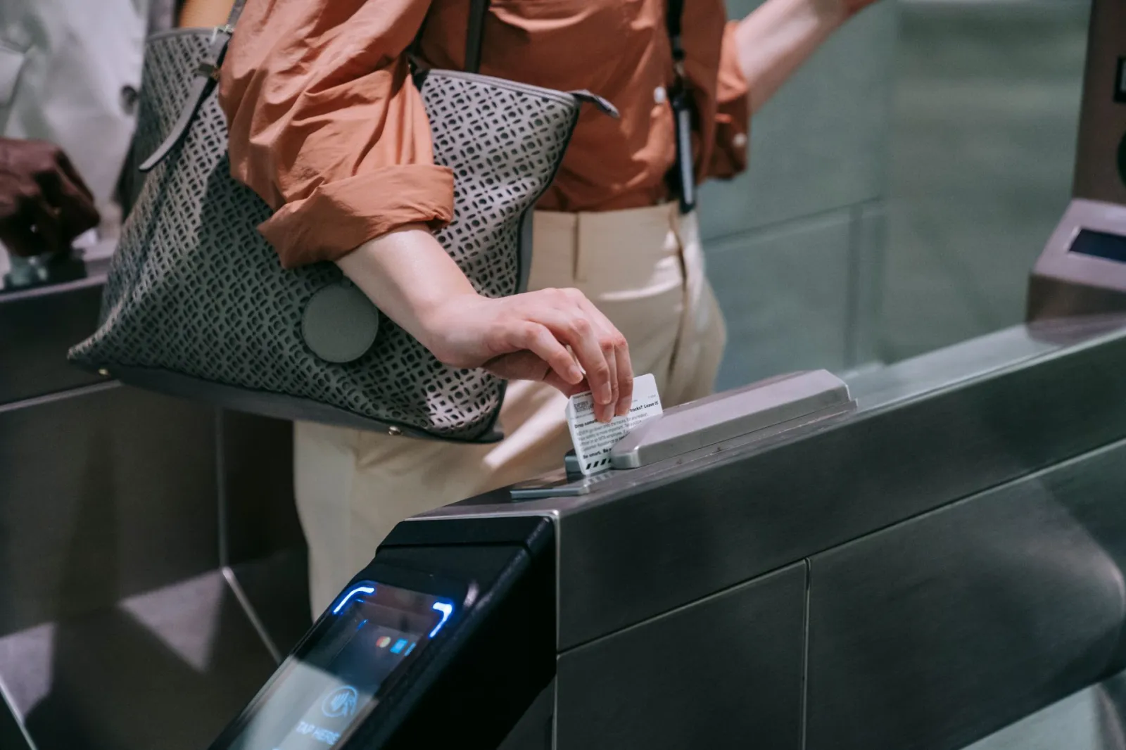 Close-up of woman using ticket at subway entrance turnstile, showcasing modern public transport system.