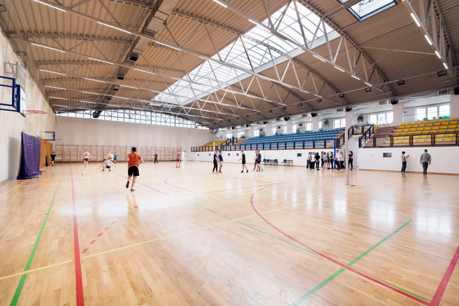 Wide-angle view of an indoor basketball court with players practicing and engaging in sports activities.
