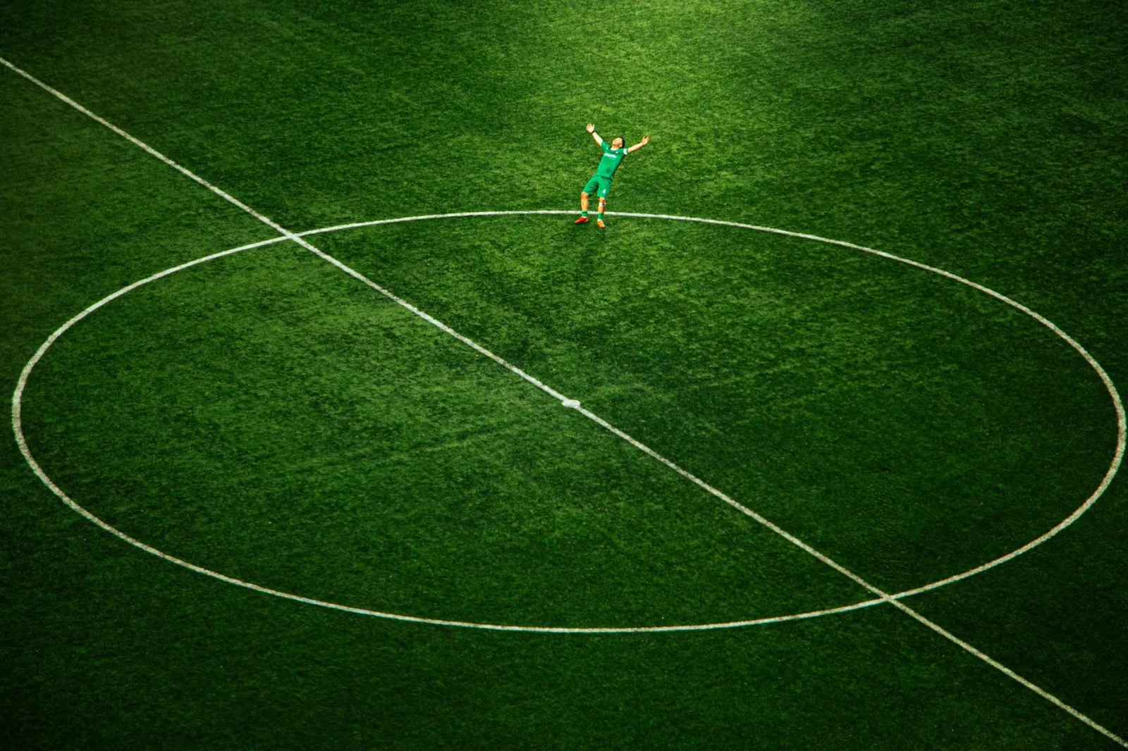 A soccer player celebrates on an empty field, spotlighted in the stadium's center circle.